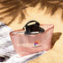 A large mesh beach tote bag in pink with black handles, containing books and sunglasses, on sand.