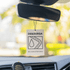 A white air freshener hanging from a rearview mirror, featuring a tear drop and road design, with a logo at the top.
