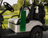 A green cotton golf towel hangs from a golf cart, with golf clubs visible in the background on a sunny course.