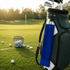 A blue cotton golf towel hangs from a golf bag beside a basket of golf balls on a grassy field.
