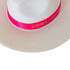 A white straw fedora hat with a bright pink band featuring a logo.
