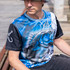 A fishing tee featuring a blue and black design with a graphic of a fish, worn by a person outdoors.
