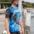 A men's fishing tee featuring a blue and black design with a fish graphic and a logo on the sleeve.