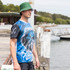 A man wearing a blue and black polyester sublimated fishing tee and a green bucket hat by the water.