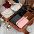 A pink toiletry bag with a handle sits inside a brown suitcase alongside clothing and a camera.