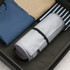 A grey multifunctional toiletry travel bag is placed inside a suitcase alongside folded shirts in blue, beige, and striped patterns.