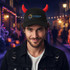 A black baseball cap with red devil horns and a logo on the front, worn by a man in a festive street setting.