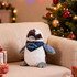 A Kookaburra plush toy in brown and grey, wearing a blue bandana, sits on a sofa decorated for Christmas.