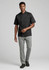 A model wearing a black short-sleeve chef jacket and grey pants, walking in a neutral background. The outfit features a logo.