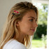 An oval acrylic hair clip in red worn in the hair of a woman with long, blonde hair. The setting is bright and outdoors.