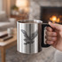 A stainless steel insulated mug with a black plastic handle, featuring an eagle design, and steaming hot contents.