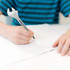 A spanner-shaped ballpoint pen in silver, being held by a person writing on a sheet of paper.