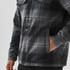 A plaid jacket featuring a grey and black pattern, with a sherpa lining and front pockets. It has a logo.