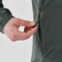 A hand adjusts the drawstring of a women's full zip jacket in green, featuring a logo on the fabric.