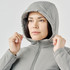 A woman wearing a light grey thermal puffer jacket with a hood, adjusting it around her face.