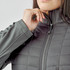 A women's grey softshell jacket featuring a quilted design and a zippered front. It has a logo on the chest.