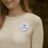 A button badge, 56mm in diameter, featuring a design with blue text and a heart shape on a white background.
