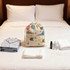 A cotton linen drawstring bag with colourful patterns, surrounded by toiletries, towels, and a pyjama set on a bed.