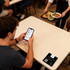 A black NFC epoxy desk tag rests on a table, alongside a customer checking a food ordering app on their phone.