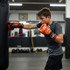 A young boy wearing red and yellow boxing gloves is training with a punching bag in a gym setting.