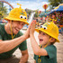 A yellow propeller hat is worn by a man and a boy, both smiling and sharing a high-five in a festive outdoor setting.