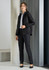 A women's black rain jacket with a hood, paired with black trousers and a white shirt. The model stands against a modern backdrop.