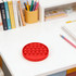 A red round fidget toy with poppable bubbles sits on a white desk beside a notebook and stationery.