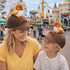 A brown baseball cap featuring a plush bird on top, worn by a woman and a child at a festive outdoor location.