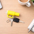 A yellow mini tumbler keyring is placed on a wooden surface next to keys, a pen, and a cup of coffee.