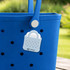 A blue tote bag features a white mini EVA holes bag charm attached to it. The charm has a handle and perforated design.