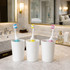 A set of three toothbrushes with blue, yellow, and pink heads in white cups on a marble bathroom counter.