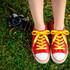 Bright red sneakers with yellow custom shoe laces resting on grass, alongside a vintage camera.