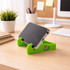 A vibrant green V-shaped stand holding a smartphone on a desk with a plant and stationery in the background.