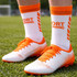A pair of white and orange sport shoes paired with orange and white woven sport socks on green grass.