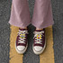Custom shoe charms in various designs displayed on burgundy sneakers, paired with light pink flared pants.