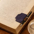 A navy blue magnetic bookmark with a pen clip resting on an open book, with a pen attached for convenience.