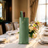 A drink bottle is nestled in an elegant green PU leather wine bag, placed on a beautifully set table.