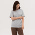 A grey t-shirt is displayed on a model, styled with loose-fitting brown trousers. The model has dark hair and a neutral expression.