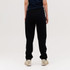 Black track pants featuring a relaxed fit, worn by a person from the back, paired with light-coloured sneakers.