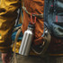 A stainless steel drink bottle is attached to a backpack with a red custom D shape camping carabiner.