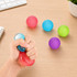 A hand squeezing a clear squishy stress relief mini ball, surrounded by coloured stress balls in red, blue, green, and purple.