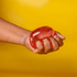 A hand squeezing a translucent red jelly cube sensory toy against a bright yellow background.