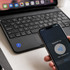 A smartphone with a dark screen is near a black keyboard, indicating NFC interaction, with a notebook visible.