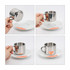 A stainless steel coffee mug with a mirror reflection, held above a white plate, showcasing its sleek design.