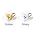 A ceramic coffee mug set with a golden and a silvery mug on matching saucers, featuring a bird design.