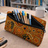 A small neoprene pencil pouch in vibrant orange and black, filled with various pens and markers, sits on a desk.