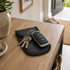 A black PU Faraday signal blocking pouch resting on a wooden table, holding a car key and some keys.