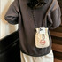 A lightweight shoulder phone bag in beige with a drawstring closure and a logo, hanging from a person's shoulder.
