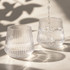 A drink bottle featuring a ribbed design, made of clear glass, with water being poured into two glasses.
