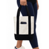 A mini canvas tote in cream with a black bottom and straps, featuring an exterior pocket.